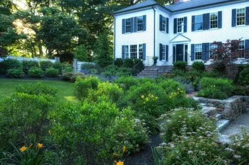 Wellesley landscape featuring a stone patio, lush lawn, mature trees, and layered garden plantings surrounding a refined outdoor living space.
