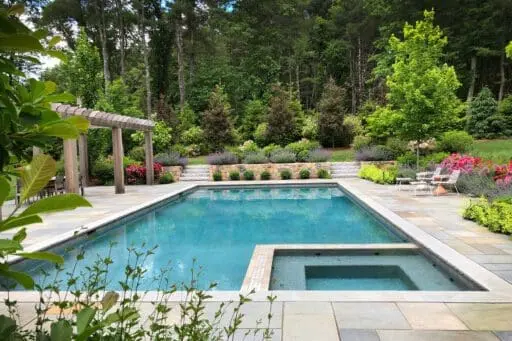 Elegant Boston-area landscape featuring a stone patio, mature plantings, and refined outdoor living details that reflect the investment involved in high-end landscape design.