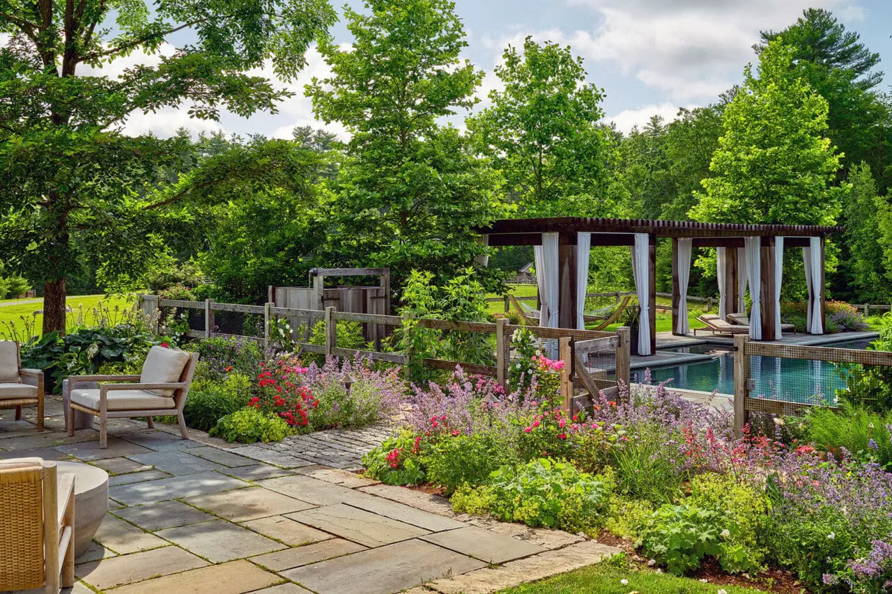 Carlisle, MA - Stone patio and outdoor lounge on a Carlisle estate, framed by layered perennial borders and mature trees overlooking the pool and pergola.