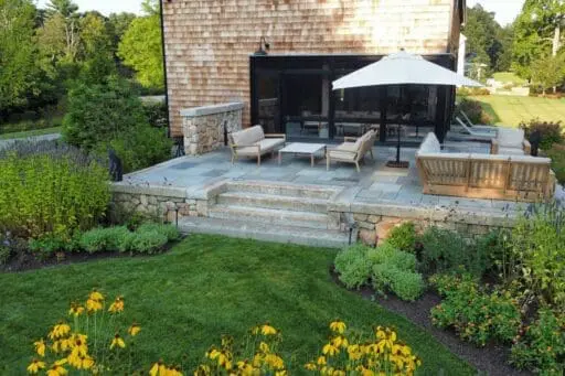 Residential patio surrounded by native perennial plantings, including yellow coneflowers, colorful flowering borders, and layered greenery around a stone terrace.