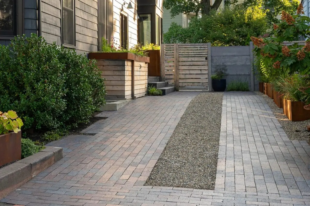 After photo of the Newton property showing the completed permeable stone driveway with a gravel center strip, new planting beds, modern planters, and updated screening.
