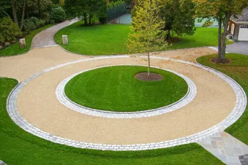 Duxbury, MA - This circular gravel driveway features a cobblestone ring and planted center island, organizing traffic flow while adding visual focus and texture.