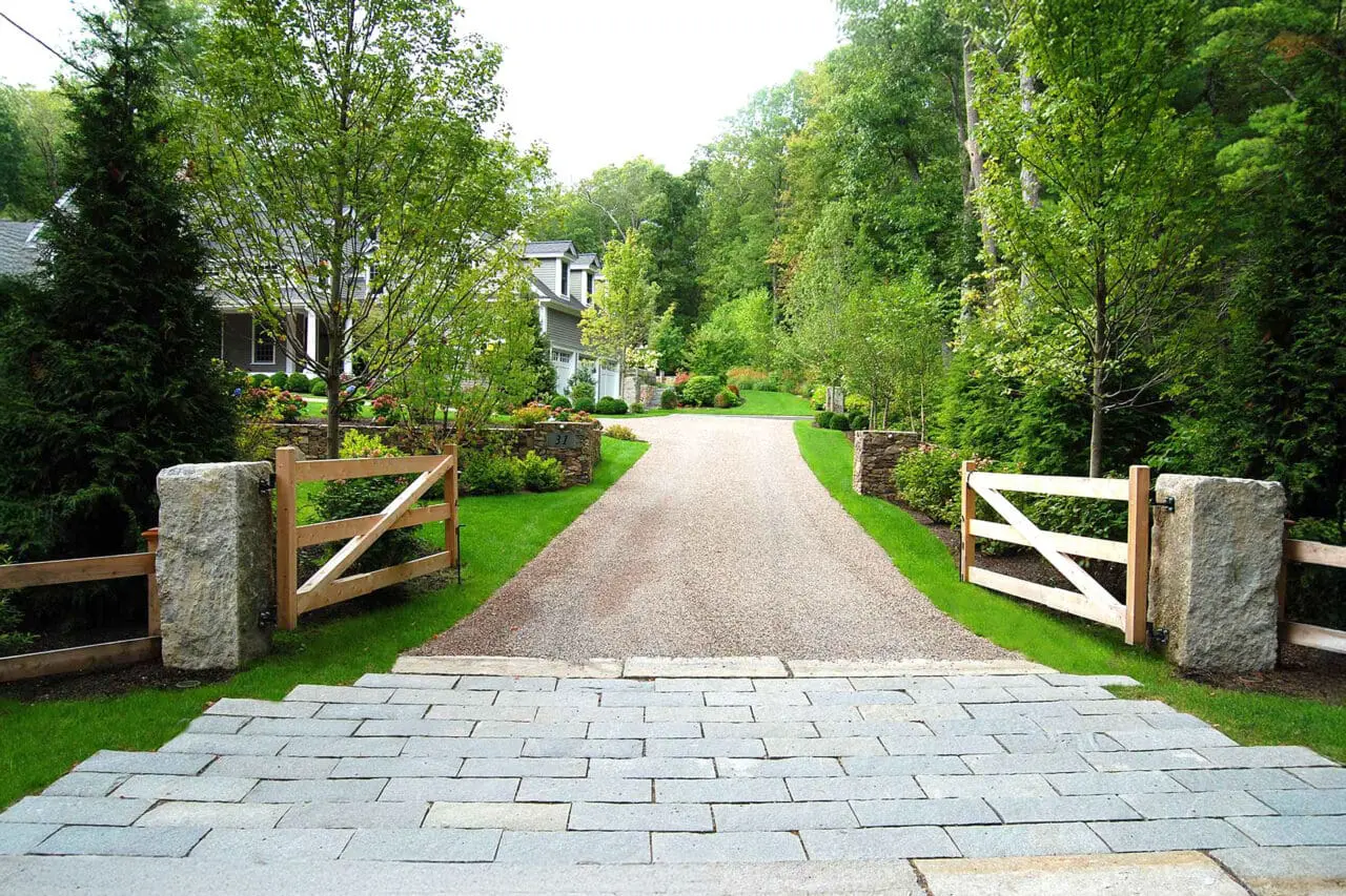Gravel surfacing meets wood entry gates and granite posts, creating a woodland driveway that balances rustic character with strong, long-lasting structural elements.