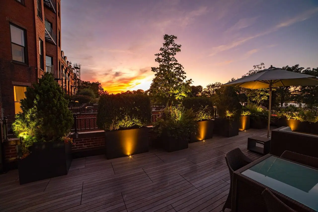 Back Bay rooftop deck with a stone patio, built-in seating, planters, and subtle landscape lighting creating a warm evening outdoor space.