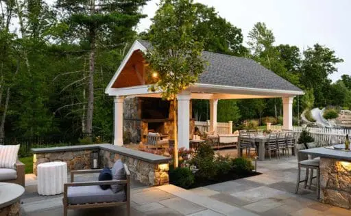 A beautifully crafted garden pavilion anchors this refined outdoor living space, creating a sheltered gathering area on a stone terrace surrounded by layered plantings and soft landscape lighting.