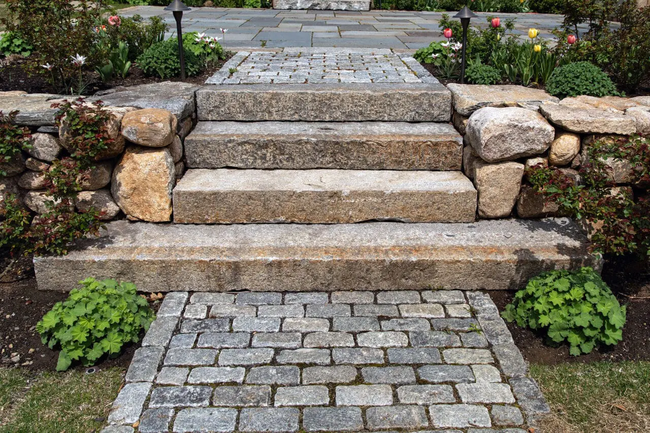 Granite steps meet a cobblestone landing, creating a refined transition anchored by fieldstone walls in Weston.