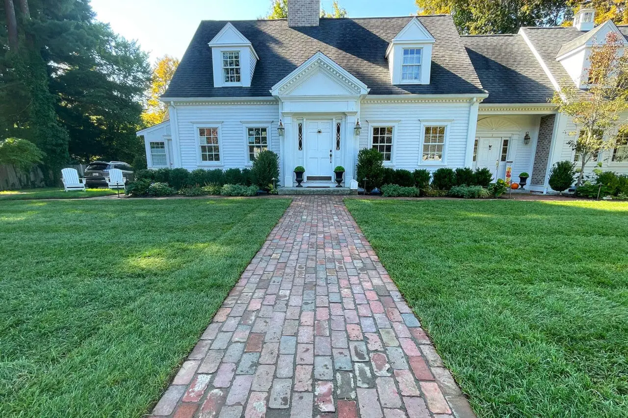 Straight reclaimed brick walkway delivers timeless curb appeal, guiding guests cleanly to the front door with warmth and New England character.