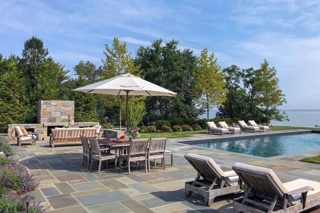 Duxbury, MA - Poolside bluestone patio with dining table and serene water views blends functional outdoor dining with scenic coastal atmosphere.