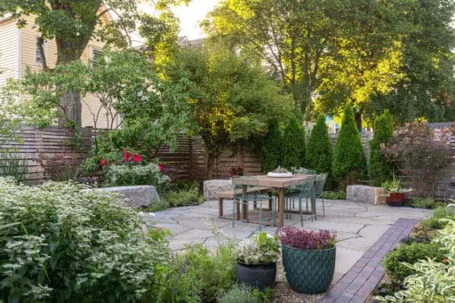 Cambridge, MA - Small garden patio with lush perennial borders and privacy trees creates a serene urban escape with natural stone paving and cozy seating.