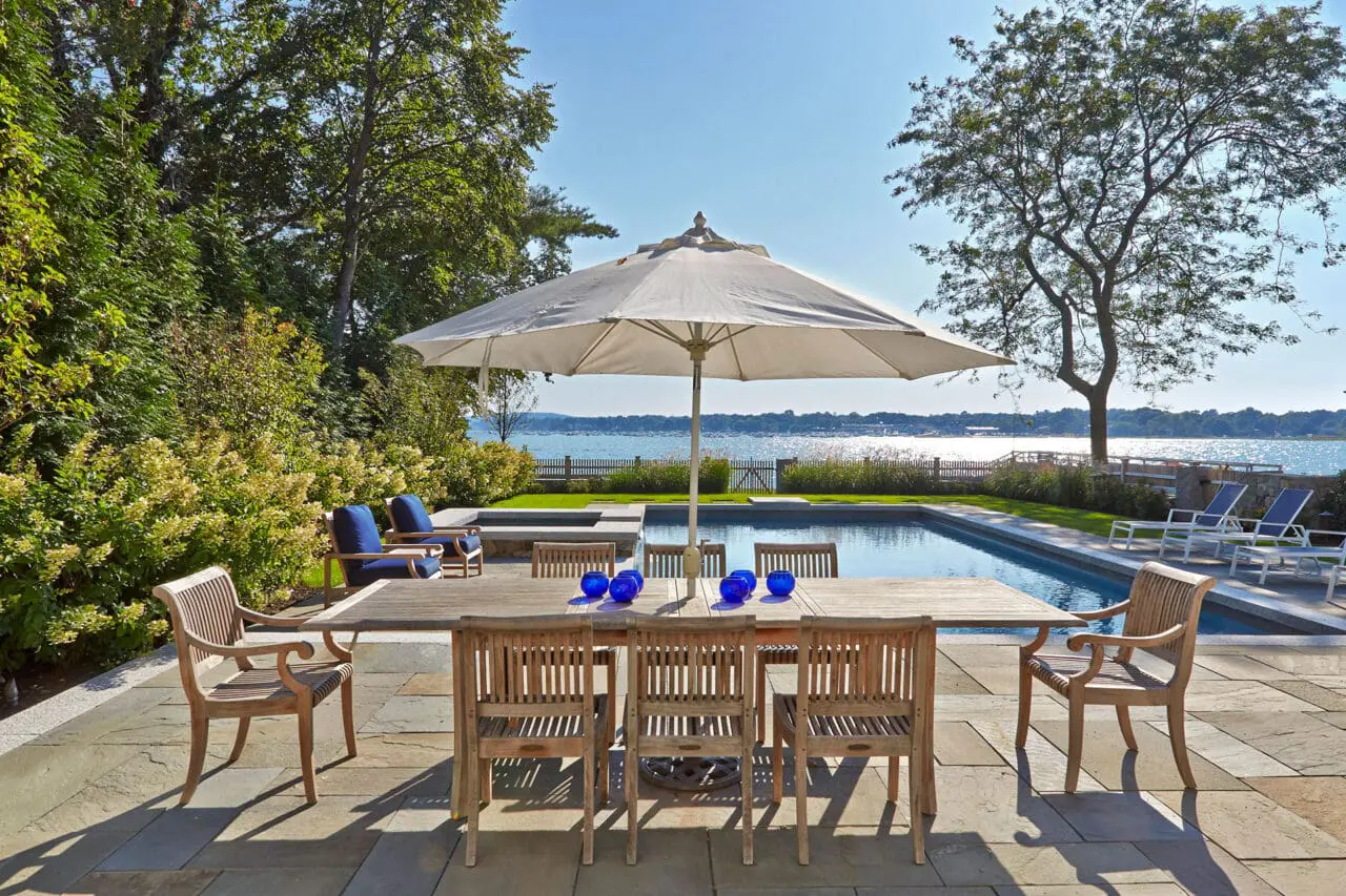 Duxbury, MA - A waterfront patio with bluestone pavers and poolside dining, capturing ocean views and seamless indoor‑outdoor flow for summer gatherings and relaxed coastal living.
