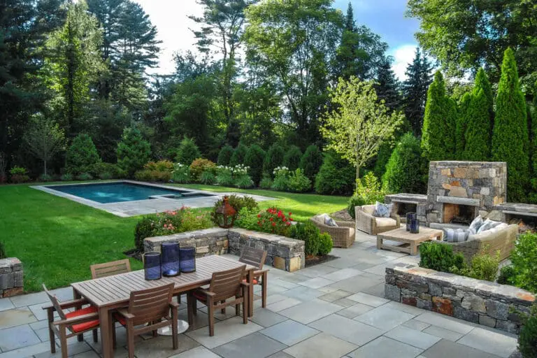 Weston, MA - A rectangular stone pool anchored by a bluestone terrace and outdoor fireplace, creating a refined entertaining space that blends structured hardscape with soft planting for year-round appeal in Weston.