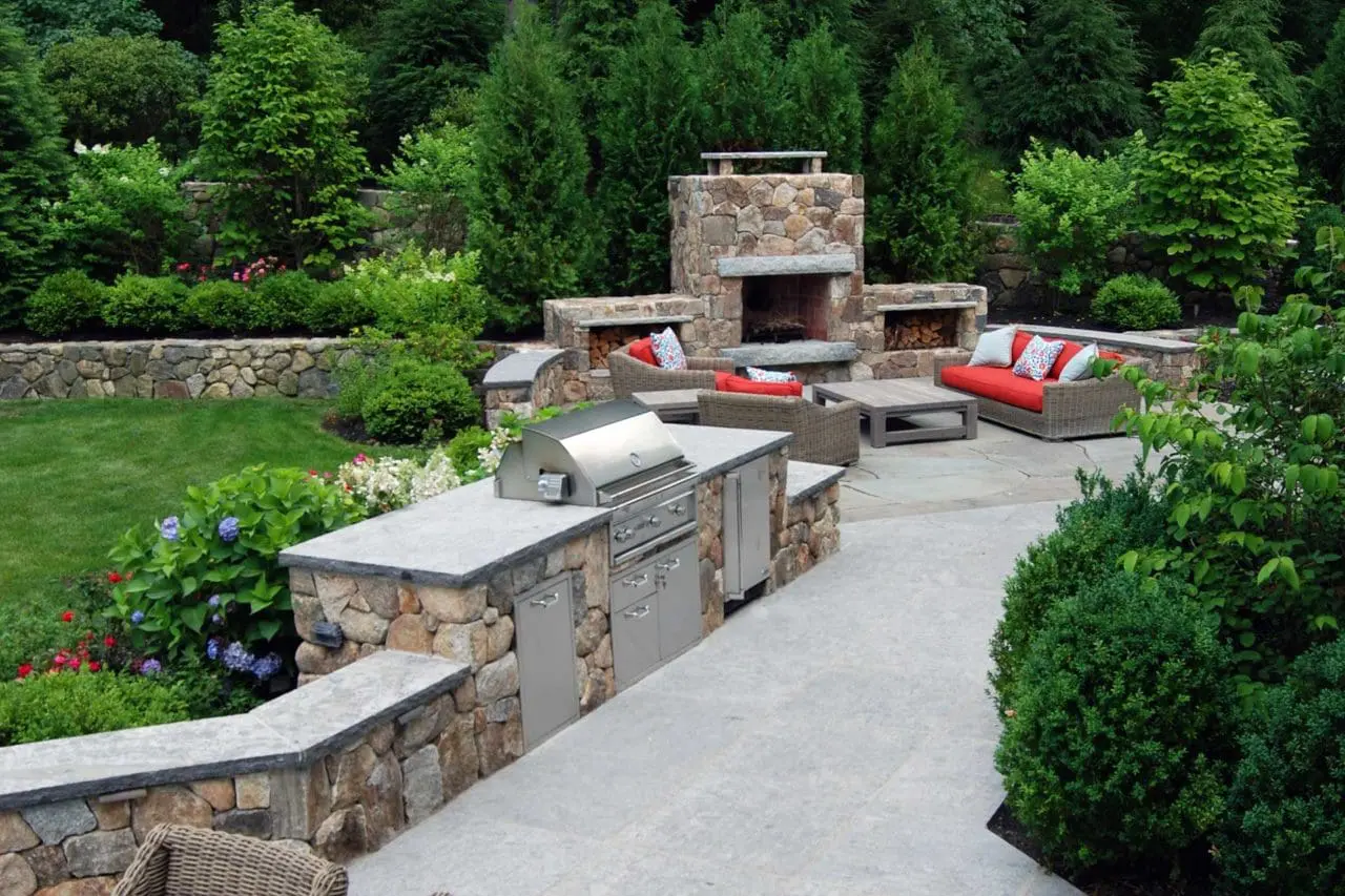 Wellesley, MA - Lush evergreen and flowering shrub plantings soften this cozy fieldstone fireplace and built in grill.
