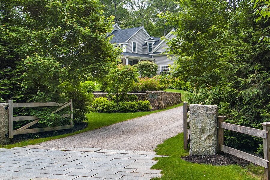 Reclaimed granite gateposts frame a gravel drive, giving this lush woodland property an established, timeless entrance.