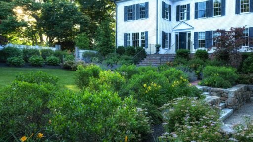 Wellesley landscape featuring a stone patio, lush lawn, mature trees, and layered garden plantings surrounding a refined outdoor living space.