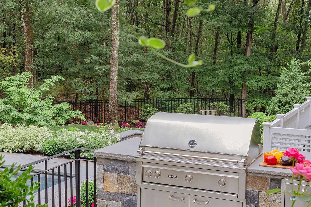 Wellesley, MA - A built-in outdoor kitchen overlooks the pool and garden, integrating cooking, circulation, and landscape views into a single outdoor living zone. photo credit: Michael J Lee