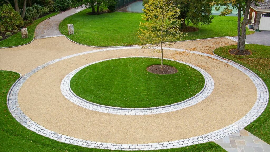 Duxbury, MA - This circular gravel driveway features a cobblestone ring and planted center island, organizing traffic flow while adding visual focus and texture.