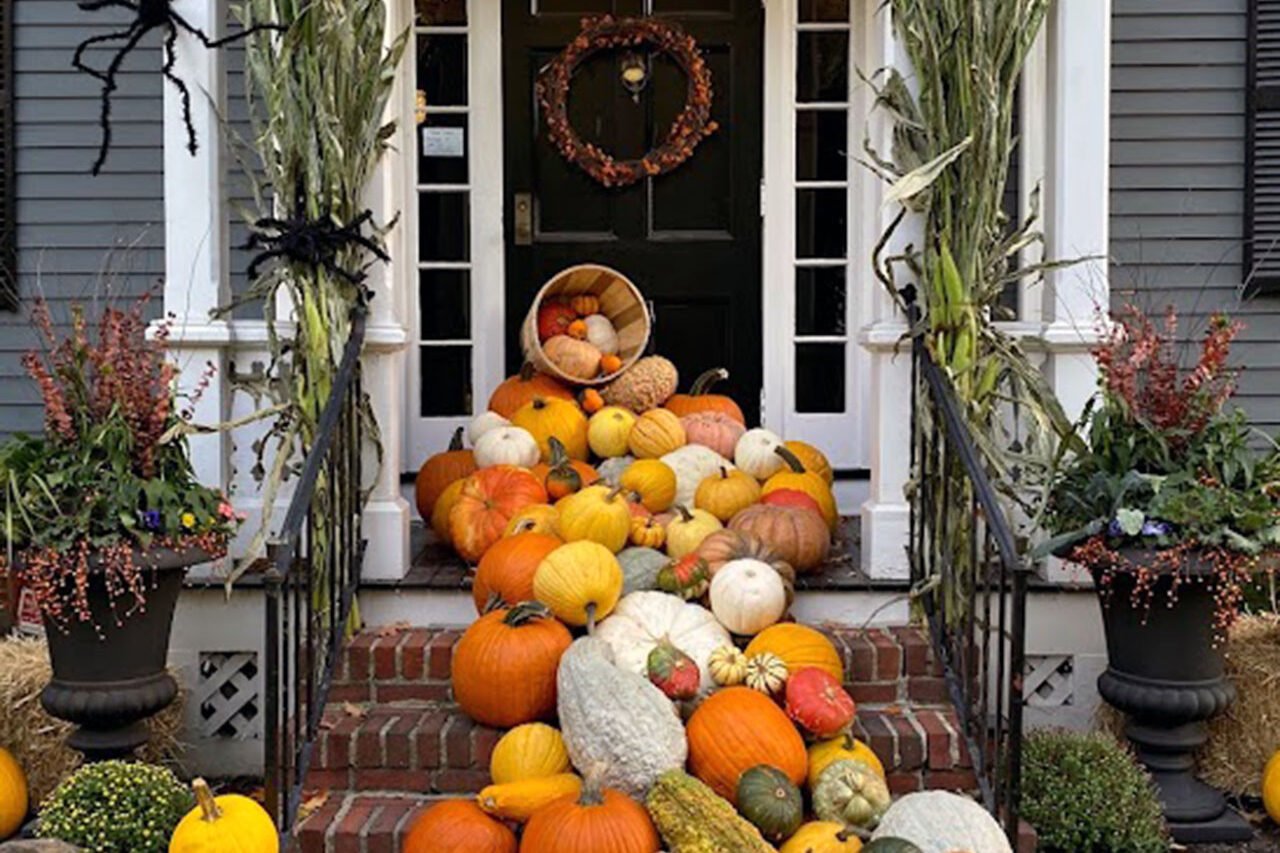 A front porch pumpkin cascade with cornstalks and spiders delivers playful Halloween energy, showing how layered props create movement and strong visual appeal.