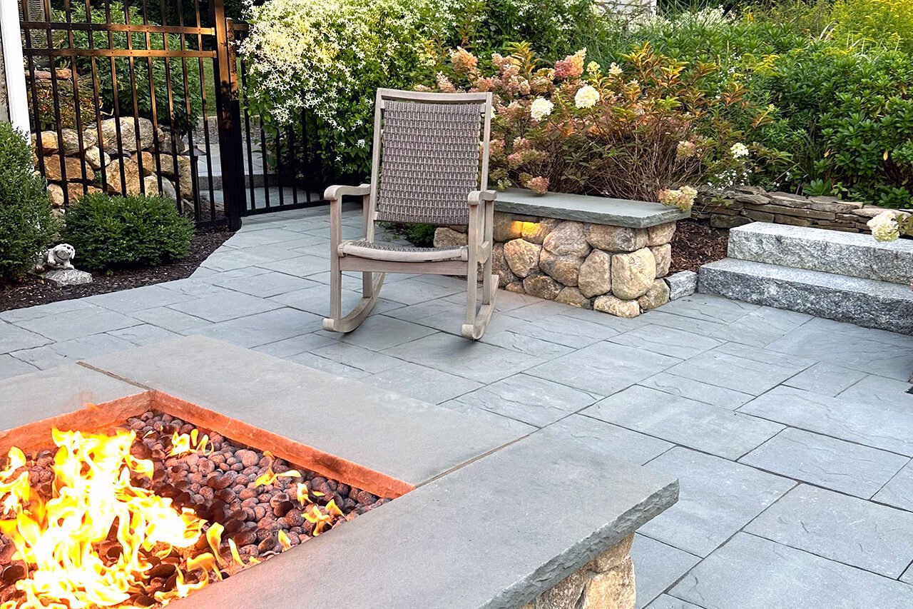 A rectangular stone fire pit set into a bluestone patio defines a cozy seating area, offering durability, warmth, and a natural focal point for everyday outdoor living.