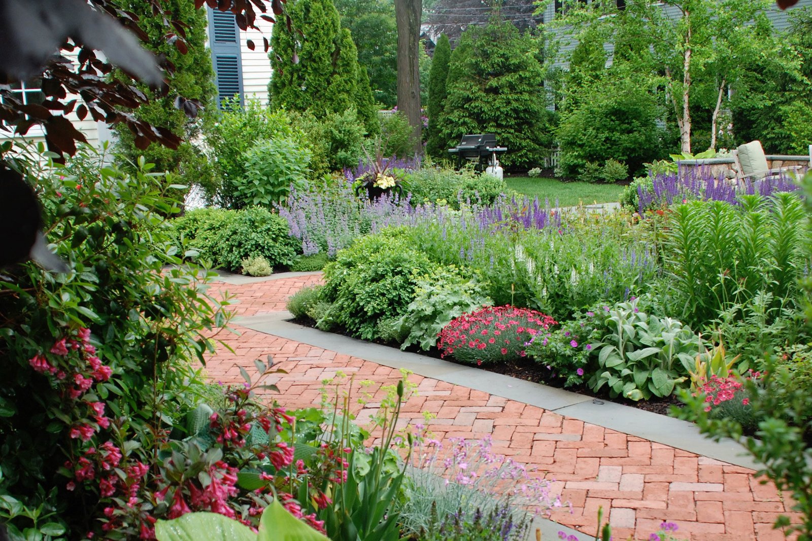 Brick and bluestone walkway weaves through perennial planting, balancing durability with New England charm.