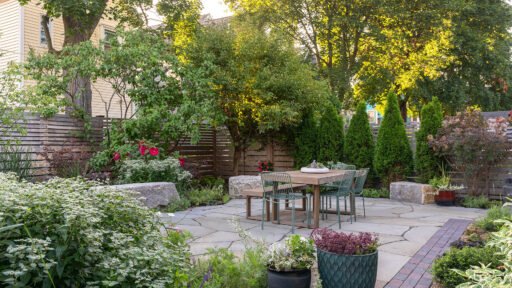 Cambridge, MA - Small garden patio with lush perennial borders and privacy trees creates a serene urban escape with natural stone paving and cozy seating.