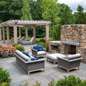 Wood pergola with stone fireplace anchors a poolside living area, enabling multi-season use and dramatic visual impact.