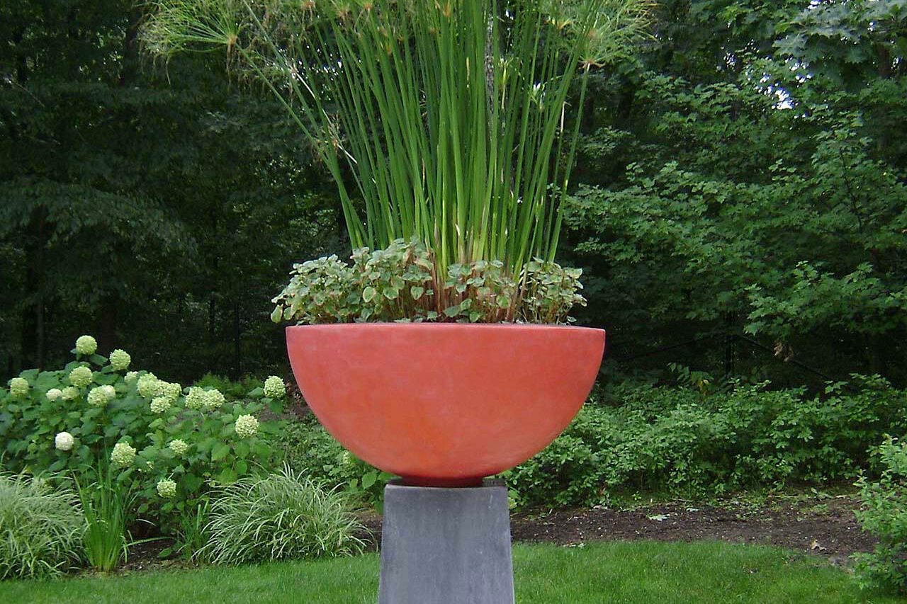 A pedestal bowl planted with ornamental grass acts as a sculptural garden feature, adding height and movement with minimal seasonal upkeep.