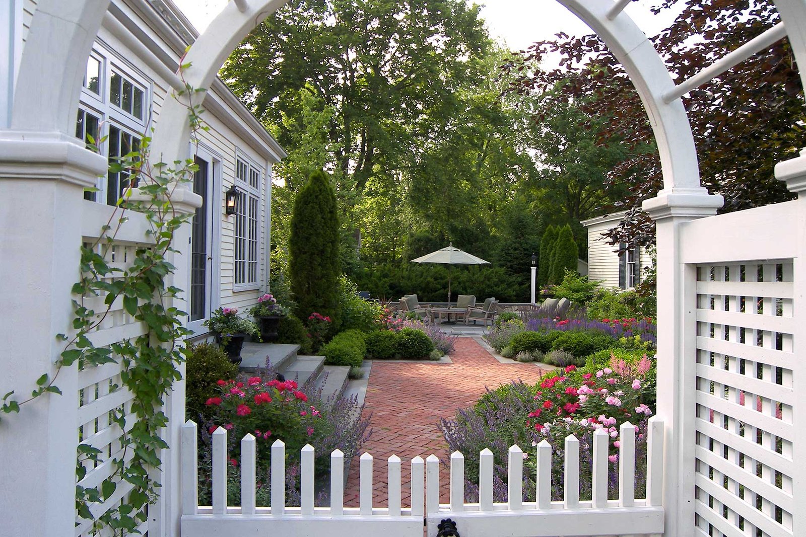 Dedham garden entry with brick path, flowering borders, and patio