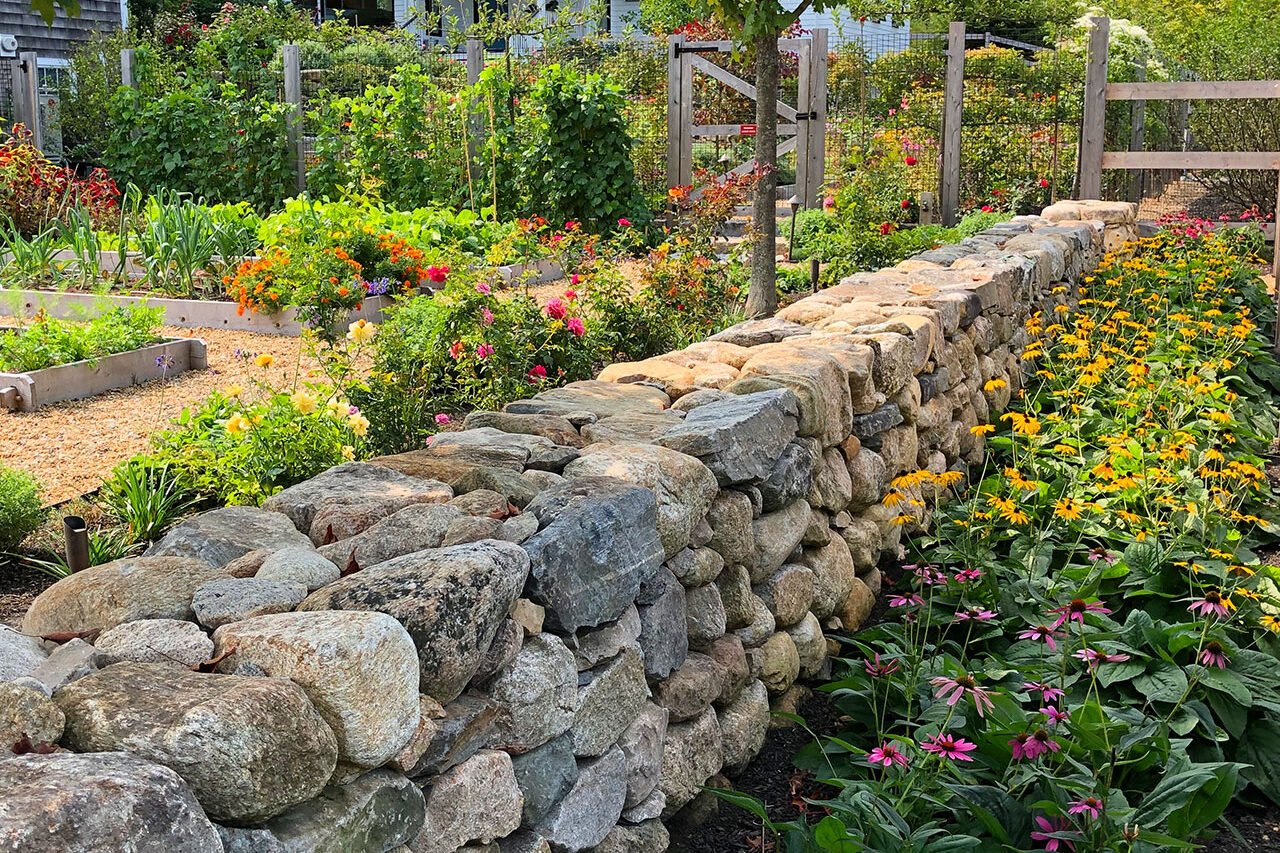 A fieldstone retaining wall runs along the fence line, using varied stone sizes to create a strong edge and clear grade transition in Weston.