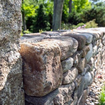 A fieldstone retaining wall manages the hillside grade, with granite steps providing a durable and clearly defined path through the slope.