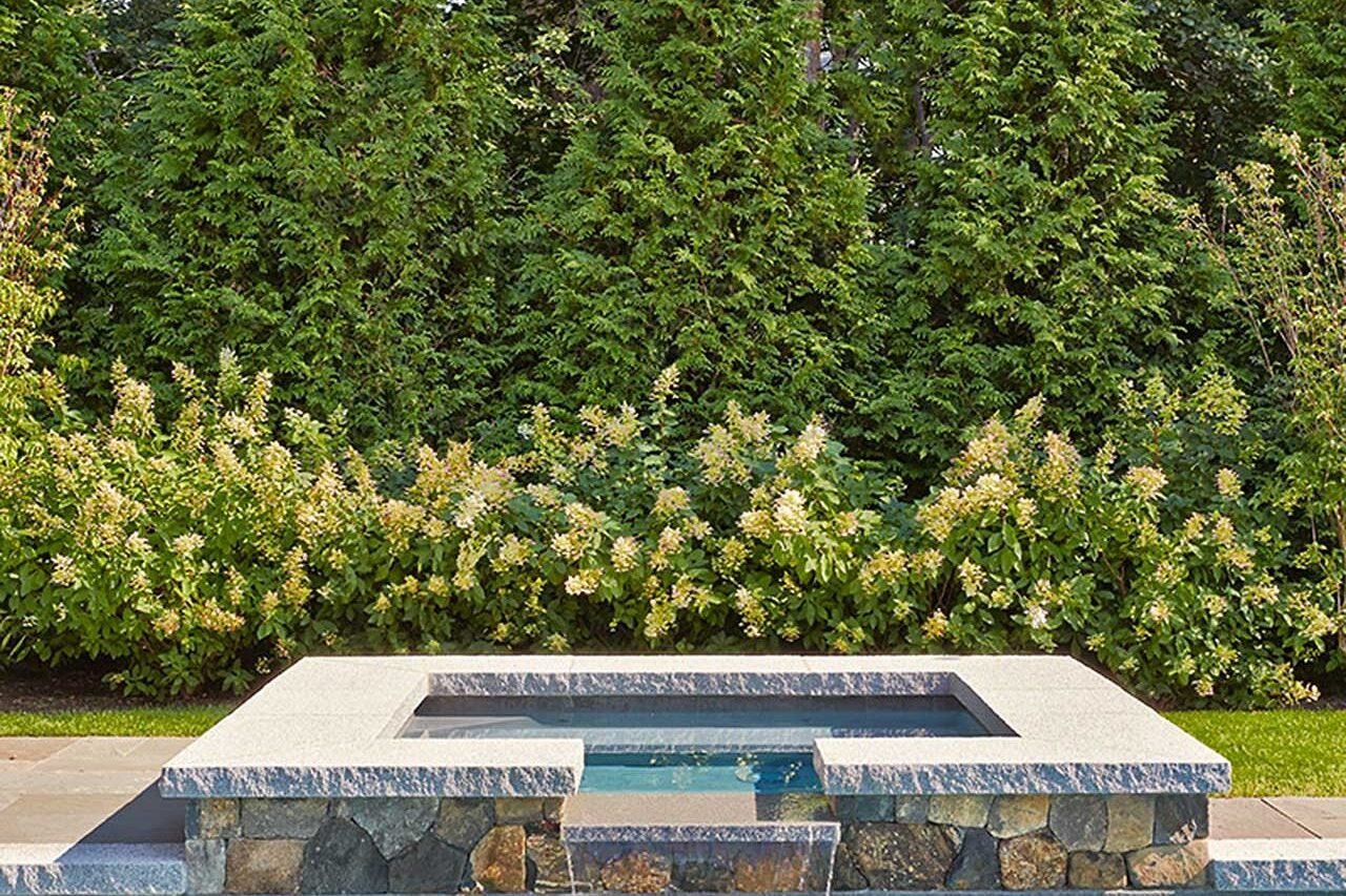 A stone spillway seamlessly connects pool and landscape, delivering gentle sound and visual flow suited to a refined coastal Duxbury setting.