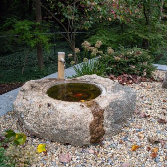 A carved granite bird bath fountain provides subtle water sound while supporting birds and wildlife, adding charm and ecological value to the garden.