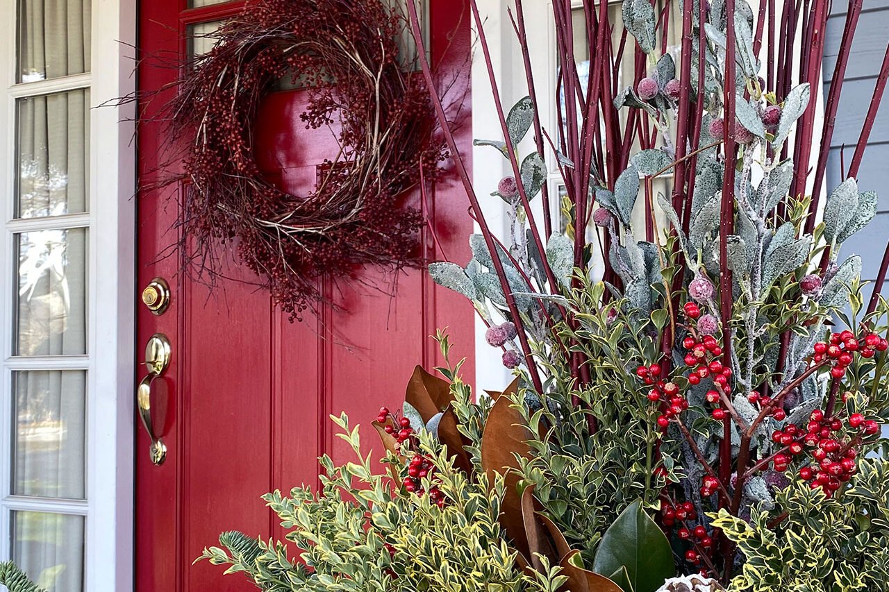 Concord entryway with a red front door decorated with a berry wreath and mixed evergreen holiday greenery.