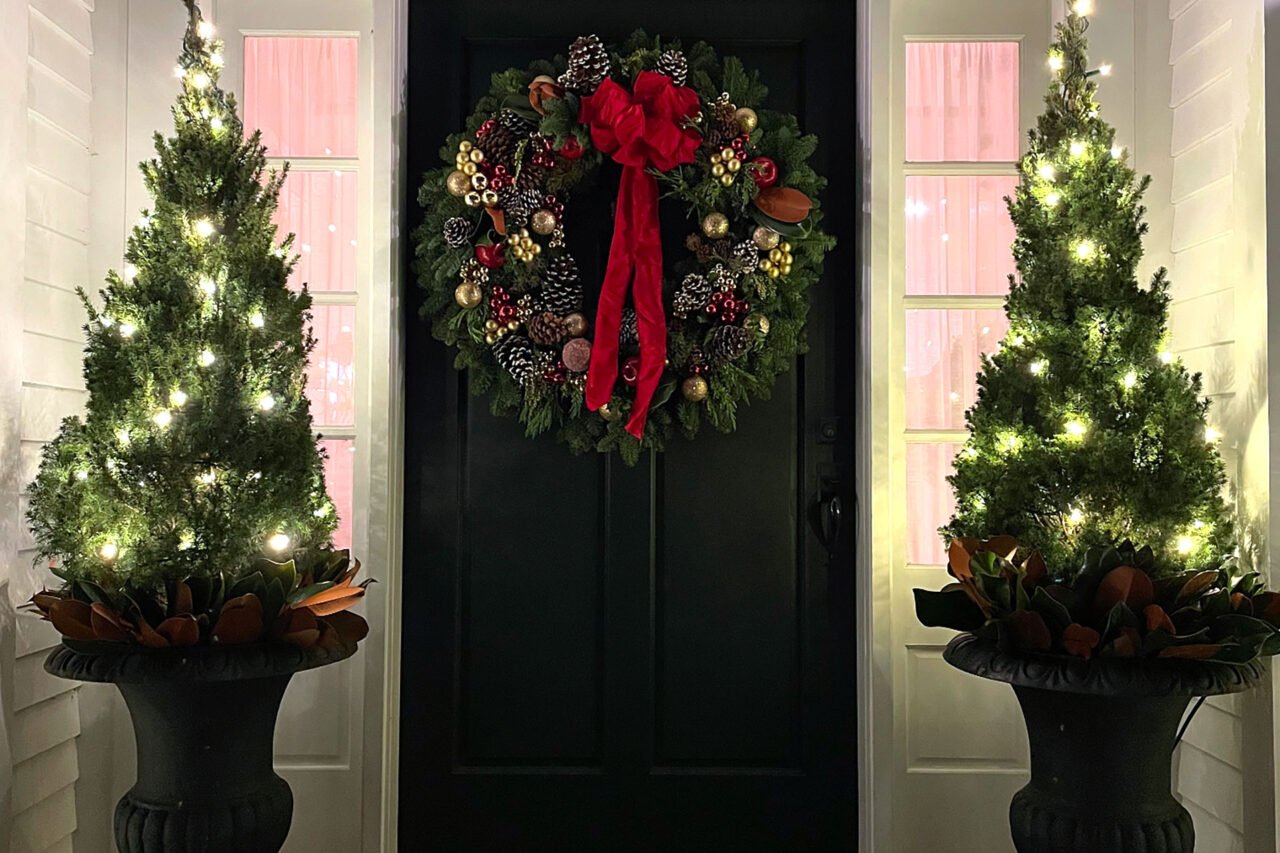 Classic Wellesley front porch decorated with a holiday wreath, illuminated evergreen planters, and warm white lights.