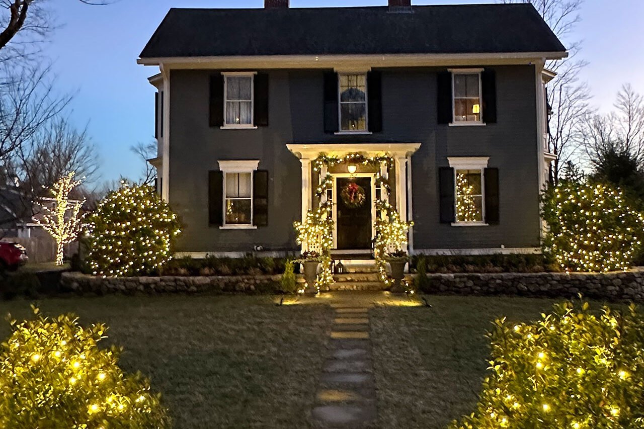 A Lincoln Colonial glows with warm white landscape lighting, highlighting the front entry and architectural details for an inviting winter evening scene.